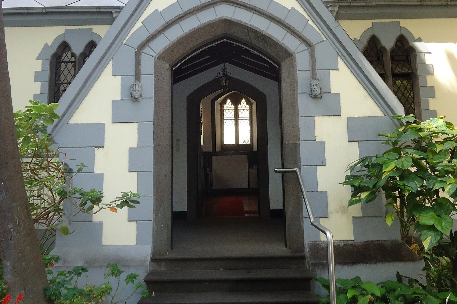 The pointed arched doorway of the church framed by grey stone blocks, with steps leading up and shrubs on either side