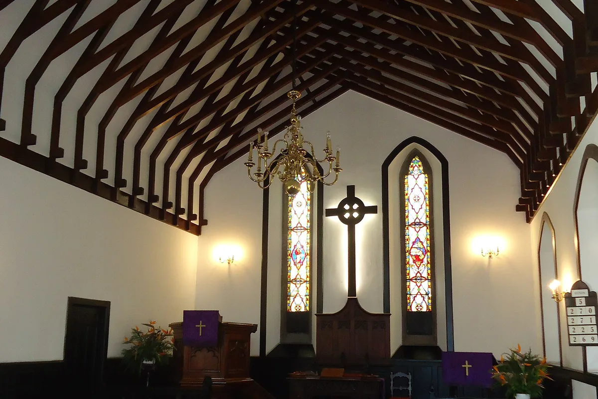 The nave of St Andrew's church in Funchal, with dark wooden pews, a red carpet in the aisle and a high timber-beamed ceiling above a cross and two tall pointed windows