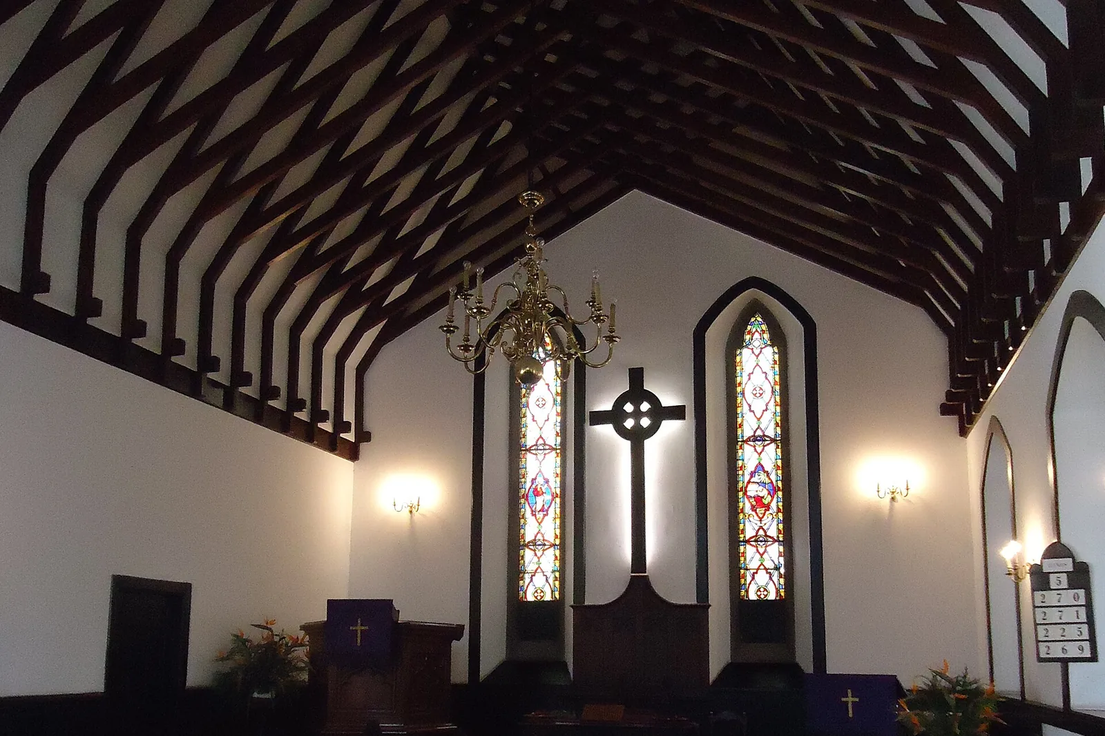 The nave of St Andrew's church in Funchal, with dark wooden pews, a red carpet in the aisle and a high timber-beamed ceiling above a cross and two tall pointed windows